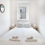 Krevet u maloj bijeloj spavaćoj sobi sa malim prozorom iznad krevera