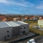 Snimka dronom s lijeve strane sivog skladišta, okruženog stambenim kućama u pozadini