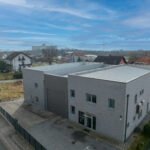 Pogled dronom s desne strane skladišta sive boje, s kućama koje okružuju područje.