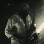 Crno-bijela fotografija saksofonista na pozornici, s blagim zelenkastim nijansama, stvarajući dramatičnu atmosferu tijekom nastupa