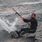 Surfer drži rukama konop padobrana i klizi po vodi